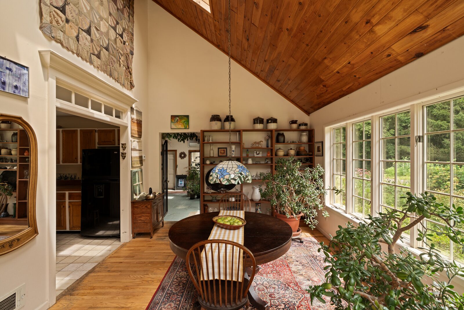 The dining room looking through to the kitchen, warm wood overhead and the stone chimney beyond