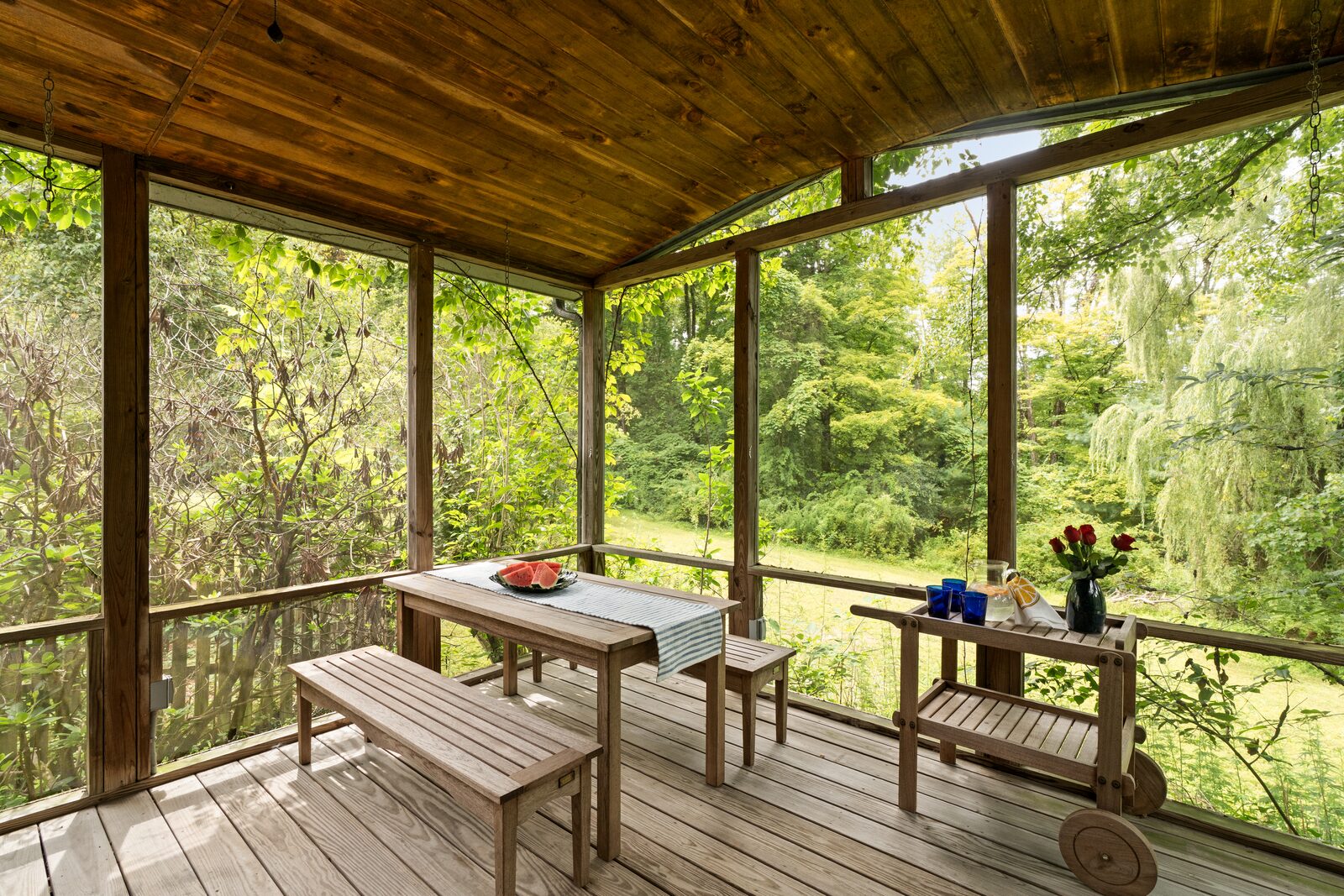 The screened three-season room — wood ceiling, screens on every side, the willow level with the floor