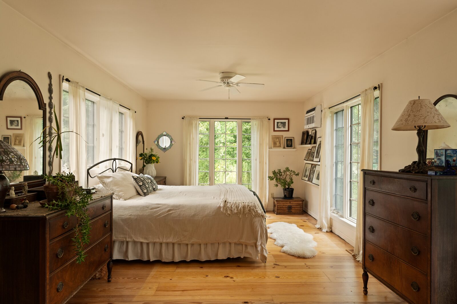 A bedroom kept simple — wide pine floors, white walls, windows doing the decorating