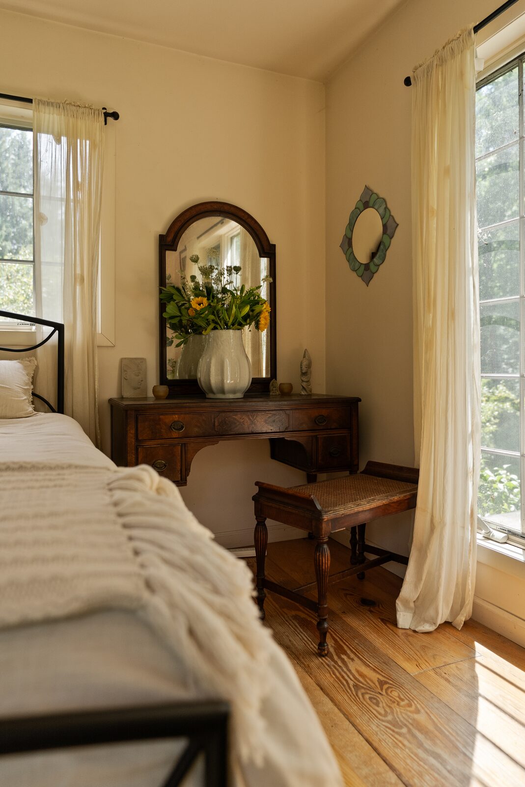 A bedroom under white walls, light coming through curtained windows