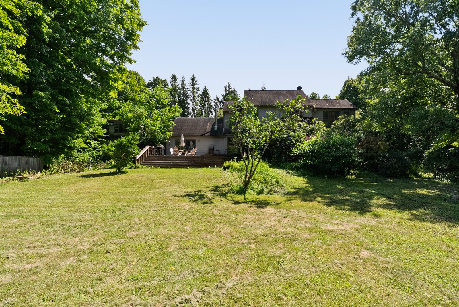 The house at the tree line, seen from across the mowed grass