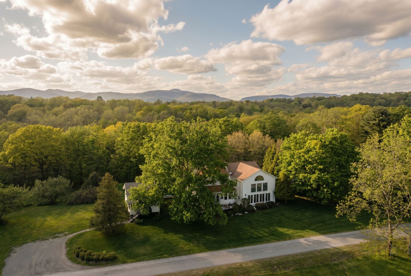 Aerial over the Hudson Valley — a home set in spring woodland with the Catskills beyond