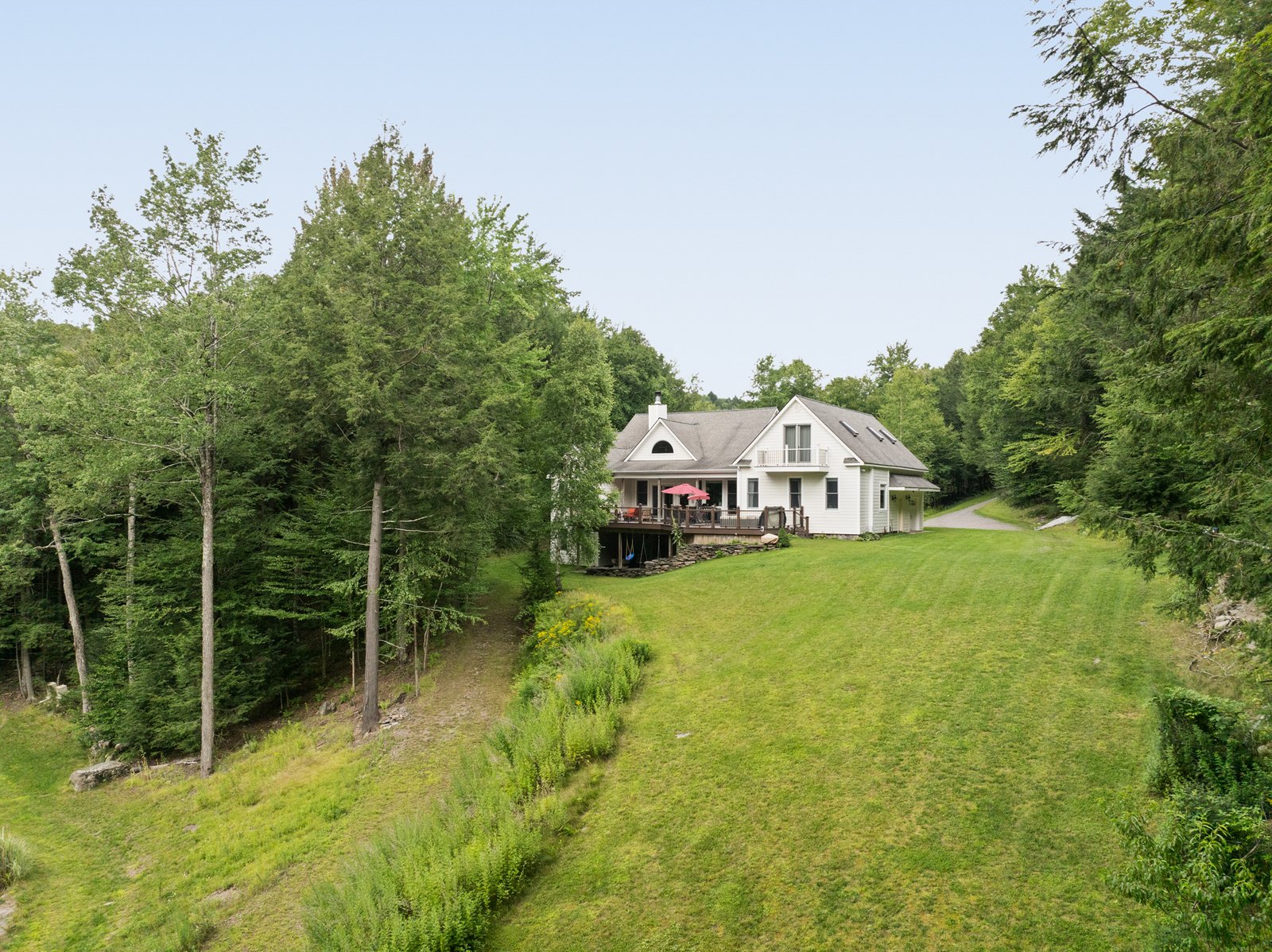 A white gabled house at the top of a mown field, framed by mature trees, Pine Hill, New York.