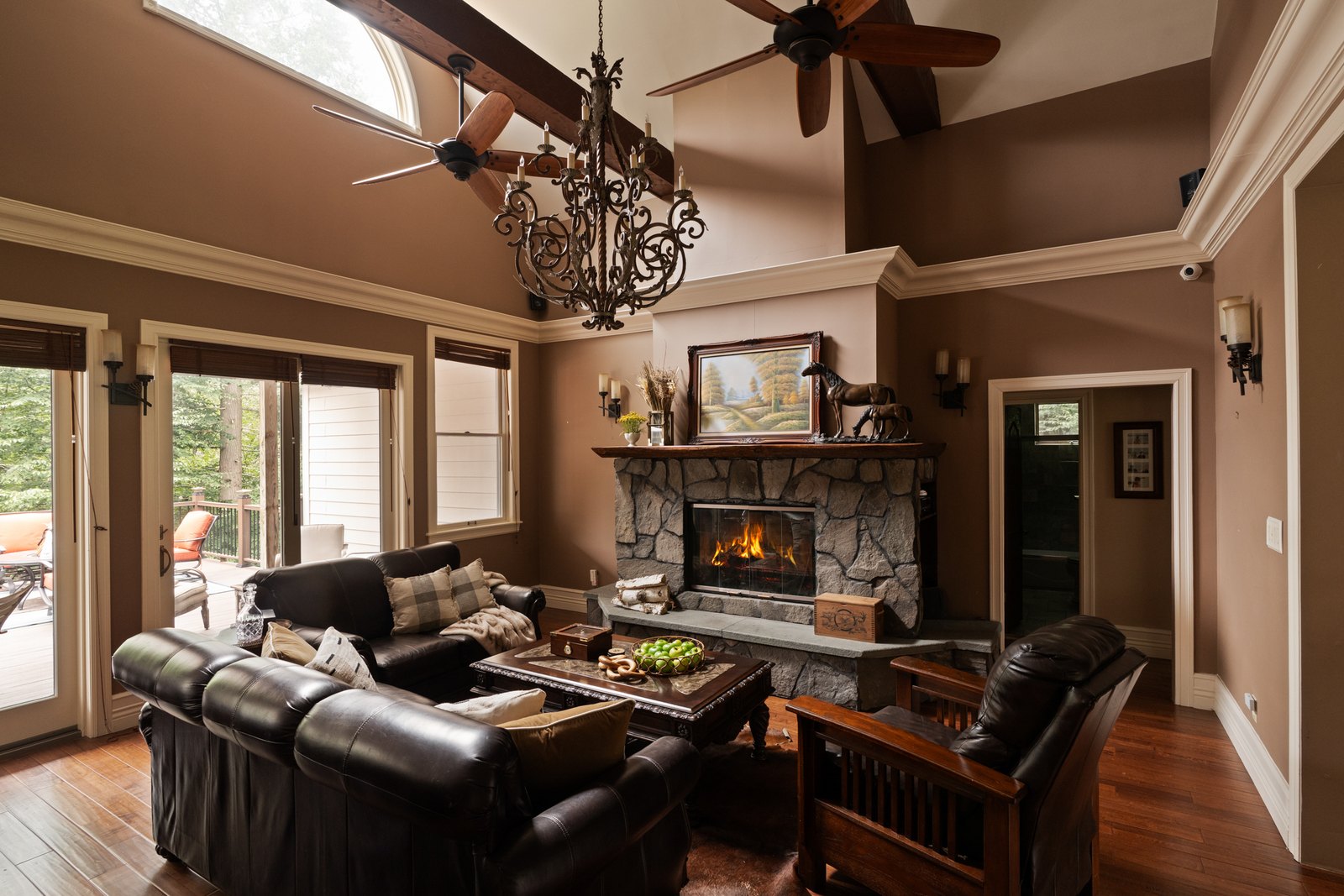 A great room rising to exposed beams with tall windows facing forest.